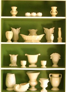 a shelf filled with white vases and bowls on top of each other in front of a green wall