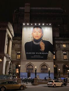 a large advertisement on the side of a building at night with cars parked in front