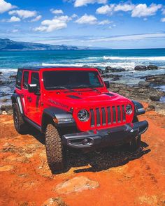 a red jeep parked on top of a rocky beach