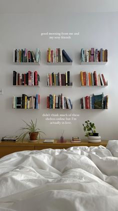 there is a bed with white sheets and books on the shelves above it that are filled with books