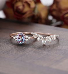 two rings with different colored stones sitting on top of a wooden table next to roses