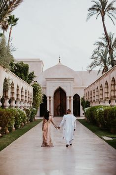 a man and woman holding hands while walking down a walkway in front of a building