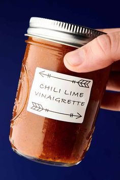 a hand is holding a jar of chili lime vinaigrette with an arrow sticker on it