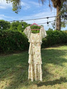 a 1970s cottage core maxi dress in cream. features little blue floral print, tiered skirt with lace trim and a pleated faux button up bodice. ties with sash in back. this dress is what dreams are made of, would be a great dress for a outdoor wedding.  dress is the second dress in default picture  in great vintage condition  with no rips or tears- a stain on bottom lace trim and a black mark on skirt (please see last pictures for closeup detail on condition) haven't taken to professional dry cleaners yet but they might be able to get it out bust 32 waist 27 length 55.5 sleeve 9 Fitted Tiered Sundress For Garden Party, Floral Print Tiered Dress For Garden Party, Bohemian Tiered Dress With Ruffles For Garden Party, Fitted Bohemian Tiered Dress, Spring Prairie Dress With Ruffles For Garden Party, Cottagecore Ruffled Dress For Vacation, Cottagecore Maxi Dress With Ruffles, Cream Tiered Summer Dress, Cream Tiered Dress For Spring