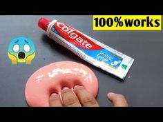 a hand holding a pink doughnut next to a tube of toothpaste on top of a table