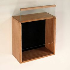 an empty wooden box with glass in it on a white wall behind the shelf is a black object