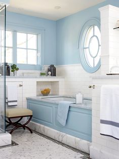 a bathroom with blue walls and white tile flooring, along with an oval window