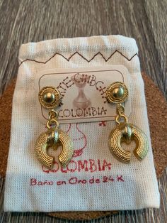 a pair of gold colored earrings sitting on top of a white cloth covered bag next to a wooden floor