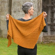 a woman holding up a yellow shawl in front of an old stone building and grass