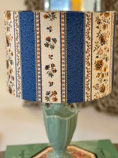 a blue lamp shade sitting on top of a table next to a green plate with flowers