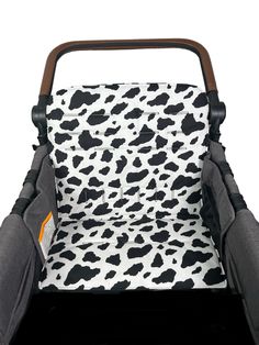 a black and white cow print baby seat cover with brown handles on it's side