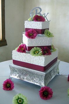 a three tiered wedding cake with purple flowers on the bottom and green daisies at the top