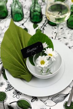 a white plate topped with a green leaf next to a glass filled with water and flowers