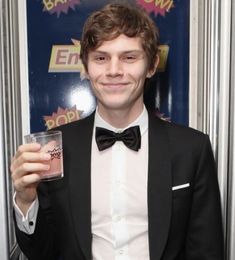 a young man in a tuxedo holding up a glass with something on it