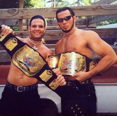 two men standing next to each other holding up their wrestling belts with the lights on