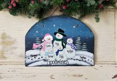 a wooden plaque with three snowmen and the words good times on it, surrounded by evergreen branches