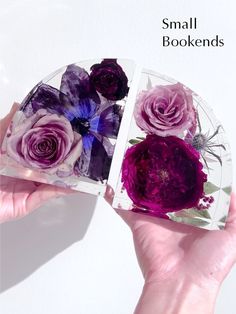 two hands are holding small glass plates with purple flowers in them and one is open to show the inside