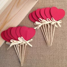 red paper hearts are arranged on top of wooden sticks and tied with white ribbon, next to a piece of wood that is laying on the floor