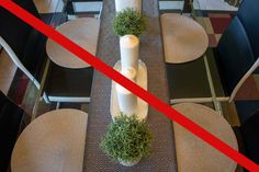 a long table with two white candles and some green plants on it, in front of a red line