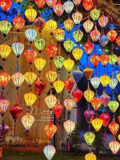 many colorful lanterns hanging from the ceiling in front of a building with lights on it