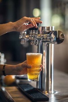 a person is filling a glass with beer from a faucet on a bar