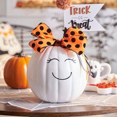 a white pumpkin with a bow on it's head sitting next to other halloween decorations