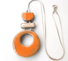 an orange and white necklace with two pendants on it's end, sitting next to a silver chain