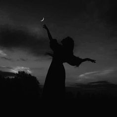 a woman reaching up into the air to catch a frisbee at night time