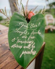 a green heart shaped sign sitting on top of a wooden table next to a vase filled with flowers