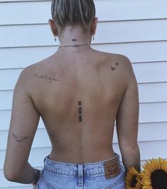 the back of a woman's body with tattoos and sunflowers in front of her