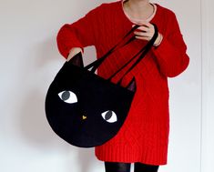 a woman is holding a black cat purse