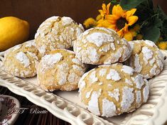 several powdered sugar cookies on a white plate next to a sunflower and lemon