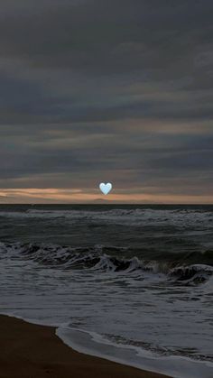 a heart - shaped object floating in the air over an ocean with waves and dark clouds