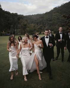 a group of people dressed in formal wear walking through the grass with one woman wearing a white dress