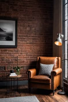 a brown leather chair sitting in front of a brick wall next to a table with a lamp on it