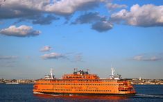 a large orange boat traveling across a body of water with clouds in the sky above