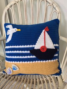 a crocheted pillow with a sailboat and seagulls on it sitting on a chair