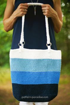 a woman is holding a blue and white crocheted bag in her hands while standing outside