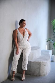 a woman leaning against a wall with her hands on her hips wearing white lace jumpsuits