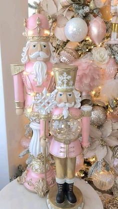 a pink and gold nutcracker next to a christmas tree