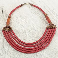 Ghana's Ila Suleyman presents a necklace featuring five beaded strands threaded with red recycled vinyl beads. The ends of the multi-strand section are finished with sese wood beads agate stones and leather strips serving as spacers. The brass hook clasp complements the beads' warm tones. The name Wend Panga comes from the Mamprusi word meaning strong will. Traditional Multi-strand Red Coral Beaded Necklace, Multi-strand Red Necklace With Wooden Beads, Multi-strand Necklace With Red Wooden Beads, Red Multi-strand Necklace With Wooden Beads, Red Fair Trade Jewelry With Round Beads, Red Fair Trade Necklace For Festival, Red Fair Trade Beaded Necklace As Gift, Red Bohemian Fair Trade Necklace, Artisan Multi-strand Red Necklaces