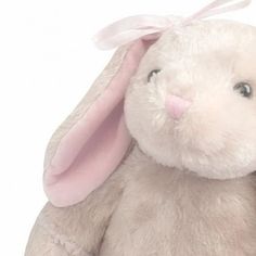 a white stuffed rabbit with a pink ribbon on its head and ears, sitting up against a white background