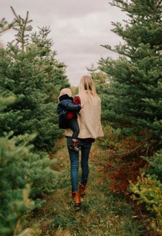 a mother and her child walking through a christmas tree farm in the woods with their back to the camera