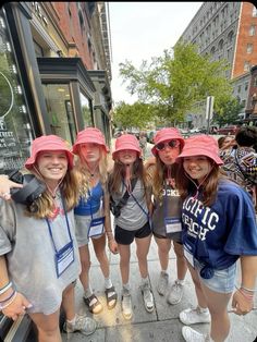 four girls in pink hats are standing on the sidewalk