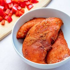 two pieces of chicken in a white bowl next to chopped red peppers