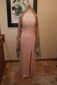 a pink dress on display in front of a framed painting and wooden table with vases