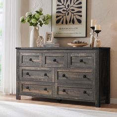 an old dresser with drawers in front of a painting and vases on the table