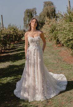 a woman is standing in an apple orchard wearing a wedding dress with floral appliques