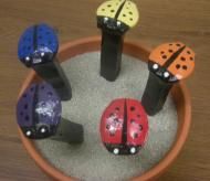 four little ladybugs are sitting in a flower pot on the table, each painted different colors