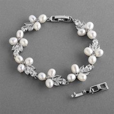 a white bracelet with pearls and leaves on the clasp is laying on a gray surface